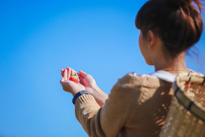 Rear view of woman holding strawberry while standing against sky