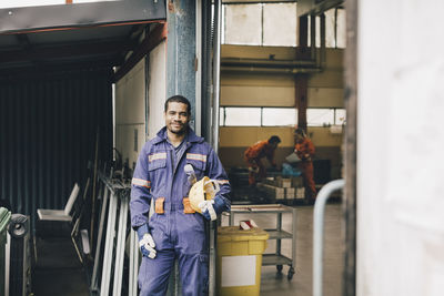 Confident male worker holding hardhat in warehouse doorway