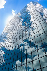  reflection of clouds blue sky in windows of glass building with sun peeking out at corner top