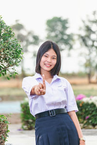 Portrait of young woman standing against trees