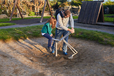 Caucasian father and daughter in school uniform playing with a bulldozer in a playground