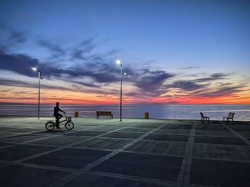 People riding bicycle on street against sky during sunset