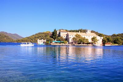 Scenic view of sea by buildings against clear blue sky