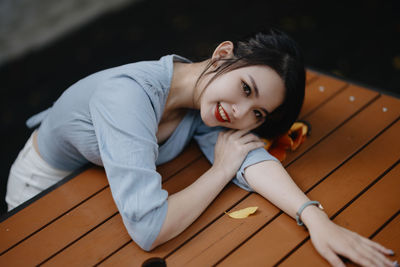 Young woman sitting on wooden wall