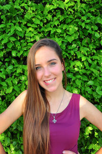 Portrait of smiling young woman with long hair against plants