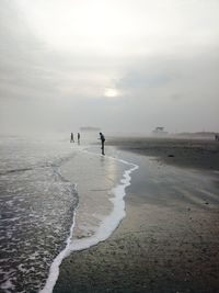 Distant view of people at beach against sky