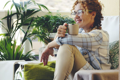 Smiling mature woman holding coffee cup sitting on sofa