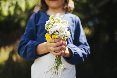 A young girl holds a bunch of wild flowers in a farm paddock