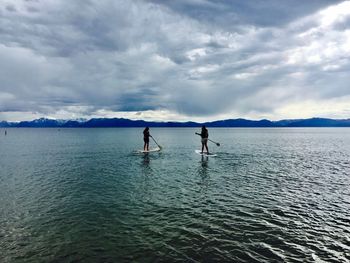 People paddleboarding in sea against cloudy sky