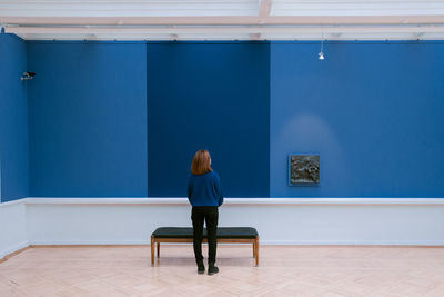 Rear view of woman sitting against blue wall