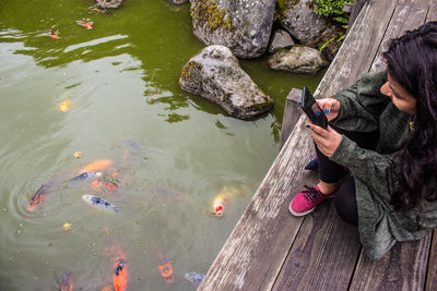 High angle view of woman photographing of fish in lake 