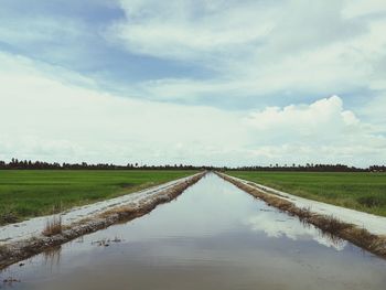 Canal amidst field against sky