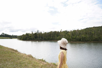 Rear view of woman by lake against sky