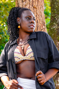 Woman looking away while standing by tree outdoors