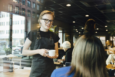 Smiling young transgender barista looking while talking with female customer in cafeteria