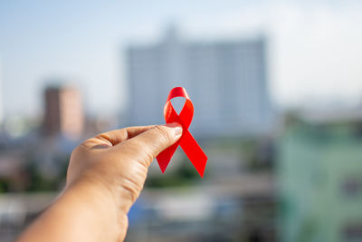 Cropped hand holding red ribbon over cityscape