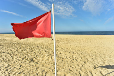 Red flag blowing in wind on flag pole stuck in sand and blue sky background