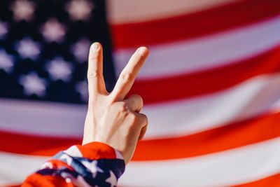 Cropped hand gesturing peace sign against american flag