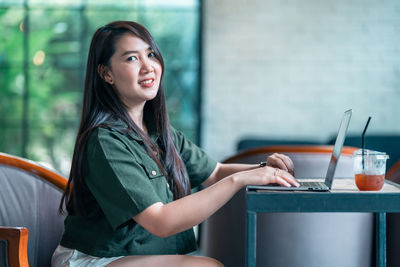 Portrait of young woman using mobile phone while sitting at home