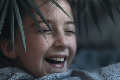 A cheerful child, a charming girl's face looking through the leaf of the plant.