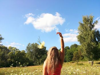 Rear view of woman with hand raised standing on grassy field against sky