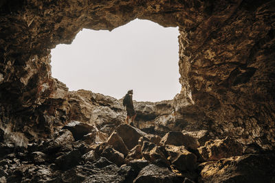 Low angle view of man spelunking cave against clear sky