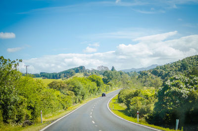Empty road along trees and landscape against sky