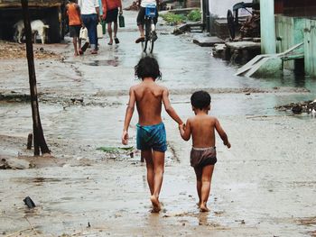 Rear view of boy and girl walking on wet footpath