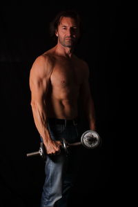 Portrait of shirtless bodybuilder man standing against black background