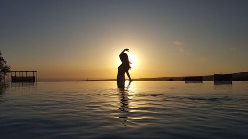 Silhouette man standing in sea against sky during sunset