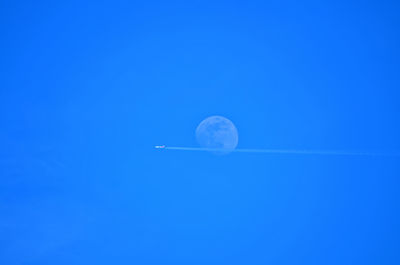 Low angle view of airplane flying in clear blue sky against moon