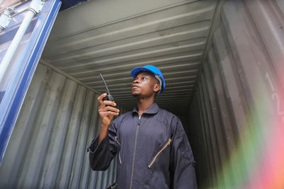 Worker taking on walkie-talkie while standing under cargo container