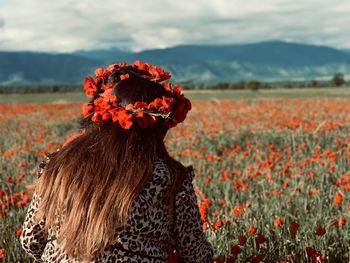 Rear view of woman standing on sunflower field against sky