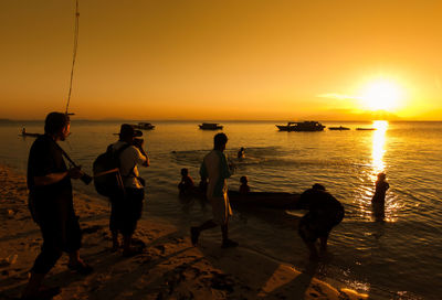 Silhouette people standing on beach against sky during sunset