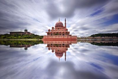 Mosque reflecting in lake against cloudy sky