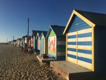 Beach huts against buildings against clear blue sky