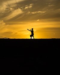 Silhouette man standing on field against orange sky