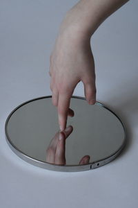 Cropped hand of person reaching towards mirror over white background