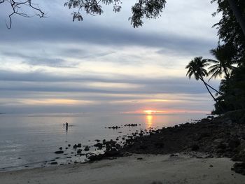 Scenic view of beach against cloudy sky during sunset