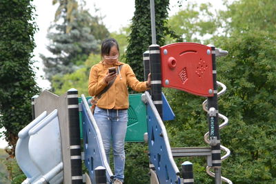 Woman using mobile phone while standing on outdoor play equipment