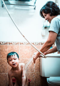 Full length of shirtless boy holding camera at home