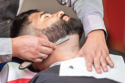 Cropped hands of barber shaving customer beard in salon