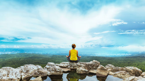 Rear view of woman standing on rock against sky