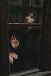 Portrait of woman looking through window in building