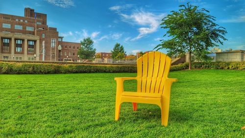 Empty bench on field by building against sky