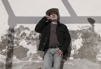 Portrait of adult man in cowboy hat and jeans against wall with sunlight and shadow. almeria, spain