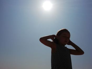 Low angle portrait of girl standing against clear blue sky on sunny day