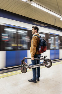 Man in stylish outfit waiting for the metro with electric scooter in the underground