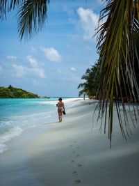 Rear view of woman walking at beach against sky