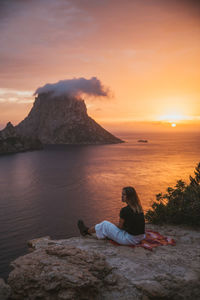 Woman sitting against sea during sunset